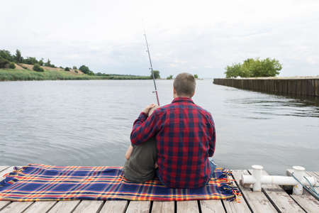 Father and son fishing. Dad shows his son how to hold the spinning and spin the reel. Fishing training on a pond or river. caring parent concept.の写真素材