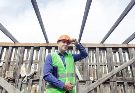 building inspector. Man in a hard hat and a yellow reflective vest examines damaged structures and inspects the building. damage assessment. Preparing for the repair or construction of a buildingの写真素材