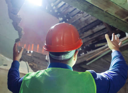 building inspector. Man in a hard hat and a yellow reflective vest examines damaged structures and inspects the building. damage assessment. Preparing for the repair or construction of a buildingの写真素材