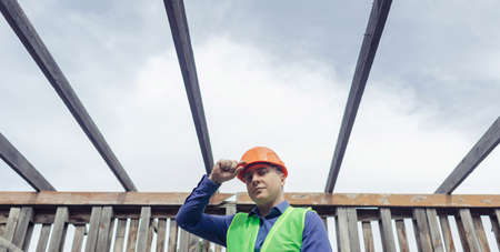 building inspector. Man in a hard hat and a yellow reflective vest examines damaged structures and...