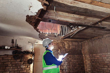 building inspector. Man in a hard hat and a yellow reflective vest examines damaged structures and inspects the building. damage assessment. Preparing for the repair or construction of a buildingの写真素材