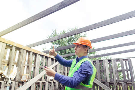 building inspector. Man in a hard hat and a yellow reflective vest examines damaged structures and inspects the building. damage assessment. Preparing for the repair or construction of a buildingの写真素材
