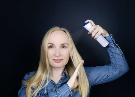 Dry shampoo. Blonde girl sprays shampoo on her hair. The problem of oily hair while traveling. An emergency remedy for excessive sebum production. Make your head clean without waterの写真素材