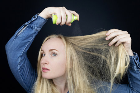 Dry shampoo. Blonde girl sprays shampoo on her hair. The problem of oily hair while traveling. An emergency remedy for excessive sebum production. Make your head clean without waterの写真素材
