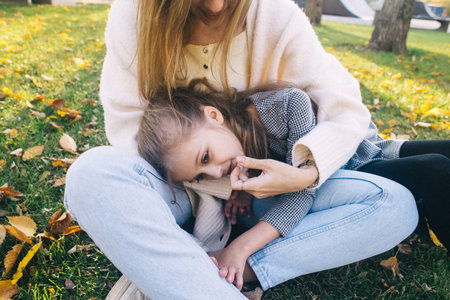 Mom and daughter in the autumn park. happy faces. Special lifestyle image processing. Sitting on the grass and yellowed leaves. Happy moments.の写真素材