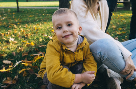 Mom and son in the autumn park. happy faces. Special processing of lifestyle images. Sitting on the grass and yellowed leaves. Happy moments.の写真素材