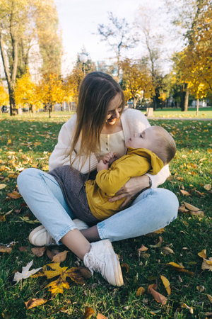 Mom and son in the autumn park. happy faces. Special processing of lifestyle images. Sitting on the grass and yellowed leaves. Happy moments.の写真素材