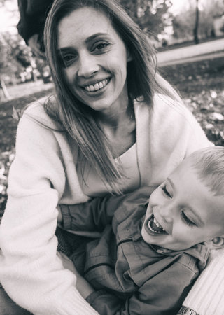 Mom and son in the autumn park. happy faces. Special processing of lifestyle images. Sitting on the grass and yellowed leaves. Happy moments.の写真素材