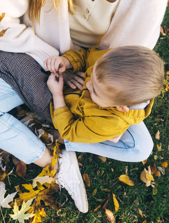 Mom and son in the autumn park. happy faces. Special processing of lifestyle images. Sitting on the grass and yellowed leaves. Happy moments.の写真素材