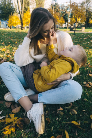 Mom and son in the autumn park. happy faces. Special processing of lifestyle images. Sitting on the grass and yellowed leaves. Happy moments.の写真素材