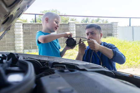 A mechanic dad teaches his son how to change the timing belt and car cooling pump at home. Child holds a pump in his hand. Maintenance of the car according to the regulations. new partsの写真素材