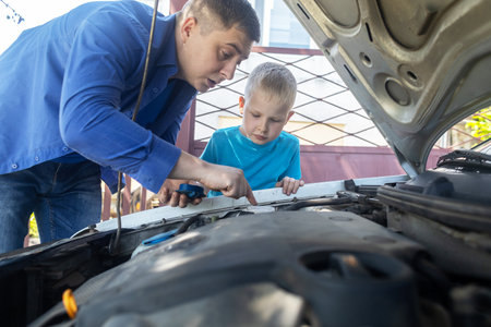 Dad shows his son where to fill in the coolant in the engine compartment. Topping up antifreeze in the car cooling system. Expansion tank near the engine. red liquidの写真素材