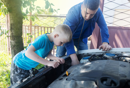 timing belt break. Man and son near hood of car is looking for a malfunction due to which the engine does not work. Driver is holding a broken front belt in his hands. Shock due to irreparable damage.の写真素材