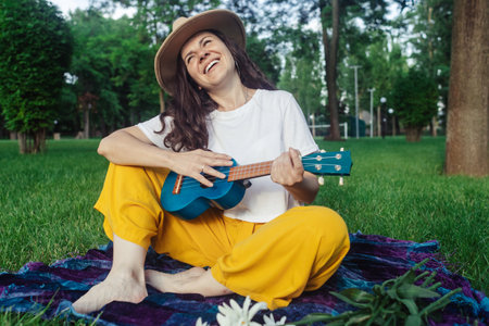 Girl in the park sitting on the grass plays the ukulele. Learning to play a four-string instrument....