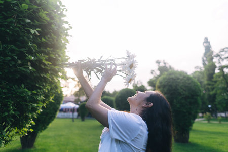 A girl in the park near a large bush sniffs a bouquet of daisies. Good luck, happy pastime, good mood. The concept of healthy relationships, mental health and self-loveの写真素材