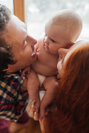 mom and dad newborn. Caring and loving parents kiss the child on both cheeks. The concept of loving parents, the manifestation of emotions and a responsible attitude towards motherhood and fatherhoodの写真素材