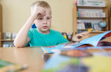 boy in library. Seven year Ukrainian guy is sitting at a table in the library and reading book....