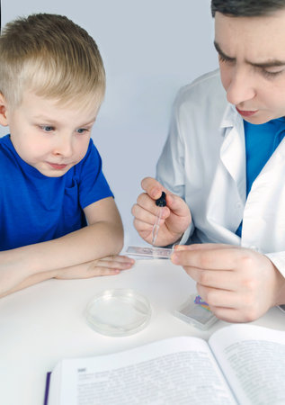 Child chemist. Teacher shows a visual experiment. A science mentor teaches an experimental approach. Microscope, petri dish, pipettes, books. Practical work in chemistry or physics. Laboratory workの写真素材