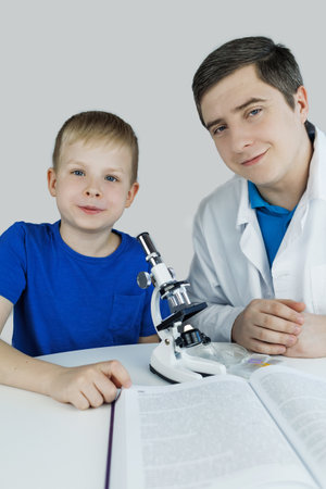 Child chemist. Teacher shows a visual experiment. A science mentor teaches an experimental approach. Microscope, petri dish, pipettes, books. Practical work in chemistry or physics. Laboratory workの写真素材