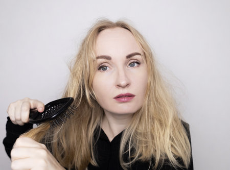 Blonde woman trying to brush her hair. Tangled curly hair without using conditioner.の写真素材