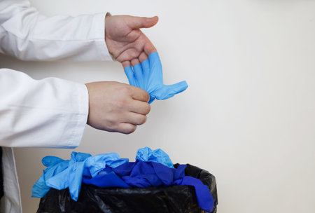 Doctor throws disposable gloves into trash bin. Medical waste disposal and treatment. Close up of medical worker's hands after work in hospital.の写真素材