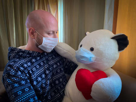 Male man guy holding teddy bear in medical mask covid-19 isolation corona virus prevention stay homeの写真素材