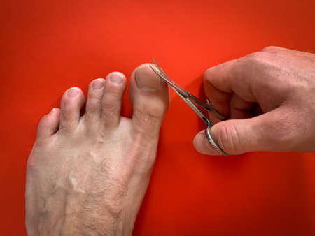 Male's hand holding on nail scissors, Man use nail scissors cutting their thumbs nail on foot toes on blue backgroundの写真素材