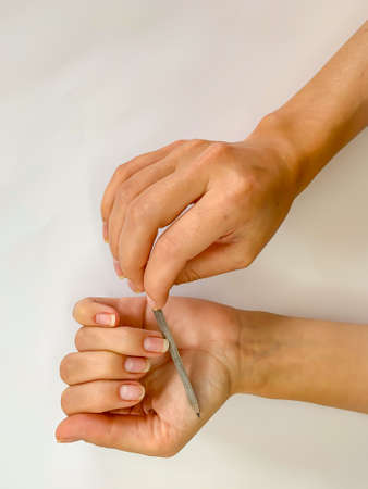 Woman's girl's hand filing nails with metal nail file on a white background. Self manicure at homeの写真素材