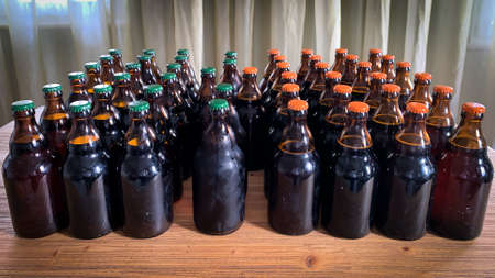 A lot of home brewery self made beer. Many brown glass craft beer bottles with green and orange corks, front view on a wooden table horizontal image.の写真素材