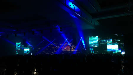 Big concert hall with a performance stage with led screen, sound and light systems full of people....