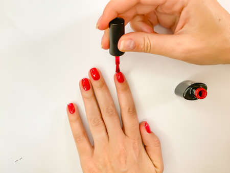 Close up female woman painting her nails with nail polish in red color on a white background. Self manicure at homeの写真素材