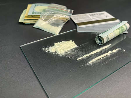 Rolled 100 us dollars, 2 lines of cocaine, plastic bag with illegal drugs and credit cards on a gray...