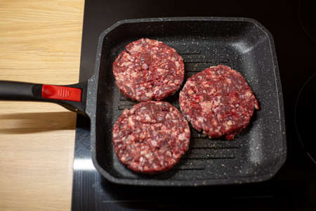 Burger raw minced beef meat cutlet on a grill pan. Process of cooking self made burgers at home.