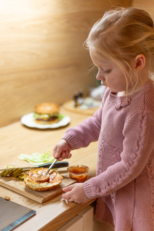 Little blond girl is cooking home made burgers in her kitchen at home.の写真素材