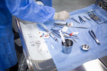 A surgeon is taking a medical tool from a tray table with dental tools, medicines and equipment...