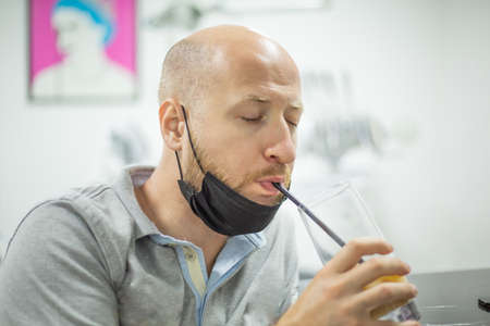 Caucasian male with mask and closed eyes is drinking his long drink with a straw.