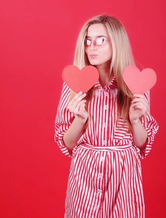 Smiling woman in red dress with paper heart in hand posing on red background. Valentine`s Day concept.の写真素材