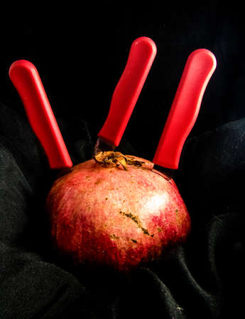 The three knives and the pomegranate on a black background