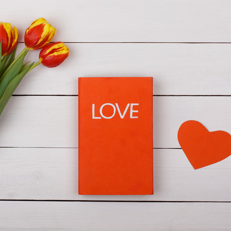 The red book Love on a white table. Flowers tulips and heart on the table.の写真素材