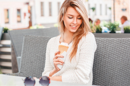 Beautiful girl sitting in a summer cafe and eating ice cream in a waffle cone. Woman hand holding waffle with ice cream.の写真素材