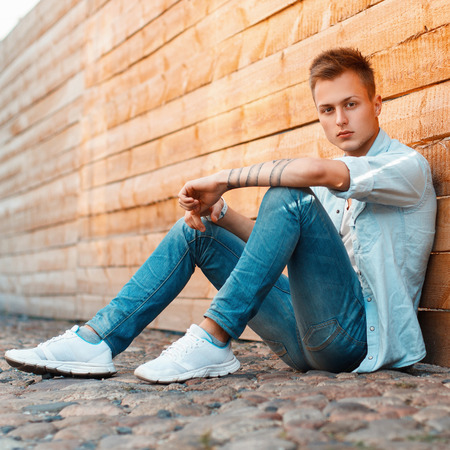 fashion man in denim clothes sitting near a wooden wall.の写真素材