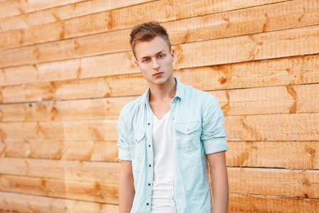 Young handsome man in a denim dress near the wooden wallの写真素材