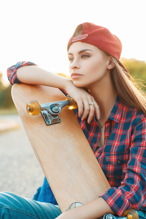 Pretty woman with skateboard in autumn day. On the background of a beautiful sunset.の写真素材