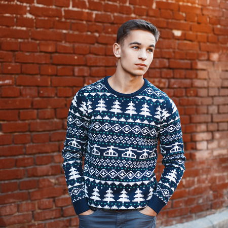 Young handsome man in a knit sweater with Christmas ornaments on a background of red brick wallの写真素材