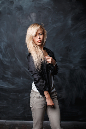 Beautiful girl with blond hair in a black shirt on a dark background with chalky stainsの写真素材