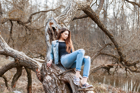 Beautiful girl in jeans jacket and denim shorts sitting on a tree. Relax in nature.の写真素材