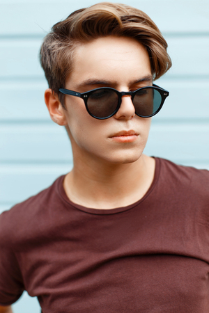 Closeup portrait of a handsome man with the hairstyle in sunglasses on a blue bright background.の写真素材