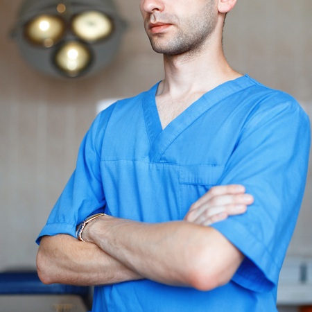 Close-up portrait of doctor surgeon in blue clothes on background of the operating lights.