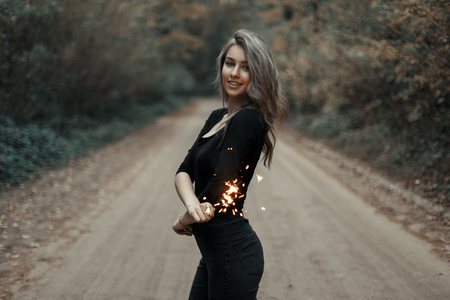 Beautiful young girl holding a sparkler in the park.