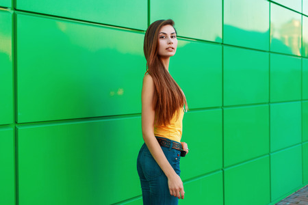 Young beautiful girl in a bright yellow shirt near the green wall.の写真素材
